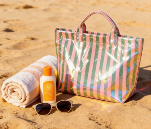 Colorful striped PVC tote bag on the beach with a towel, sunscreen, and sunglasses.