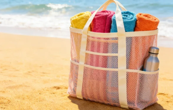 Large mesh beach bag packed with colorful rolled towels on the sand.