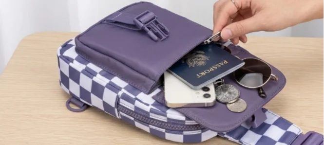 Open purple checkered sling bag with passport and phone.