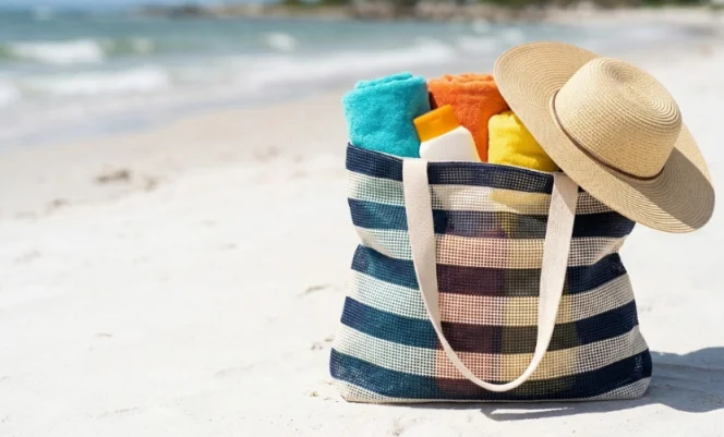 Striped mesh beach bag filled with essentials on sunny sand.